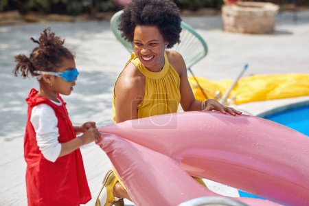 Téléchargez les photos : Jeune femme afro-américaine avec sa fille près de la piscine avec anneau gonflable se préparer pour les activités d'été. Famille, maison, style de vie concept. - en image libre de droit