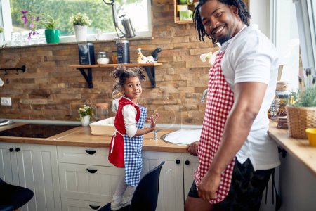 Foto de El padre afroamericano y su hija se reúnen para abordar la tarea de lavar los platos. Están lado a lado en el fregadero rodeados de burbujas de jabón. - Imagen libre de derechos