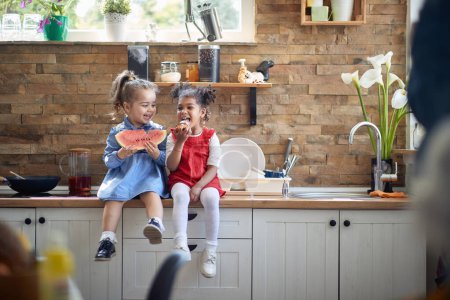 Photo for Two toddler girls come together.One girl takes a bite of a delectable muffin, while the other relishes a refreshing piece of watermelon, their smiles radiating pure delight. - Royalty Free Image