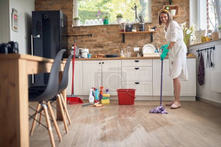Téléchargez les photos : Attrayant jeune femme au foyer humide nettoyer le sol dans la cuisine, le nettoyage de la maison. Accueil, hygiène, mode de vie concept. - en image libre de droit