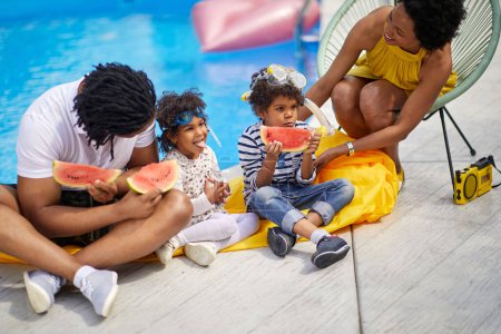 Photo for Lovely family of four sitting by the pool eating watermelon slices together. Mother and father with their two kids. Family, lifestyle, vacation concept. - Royalty Free Image