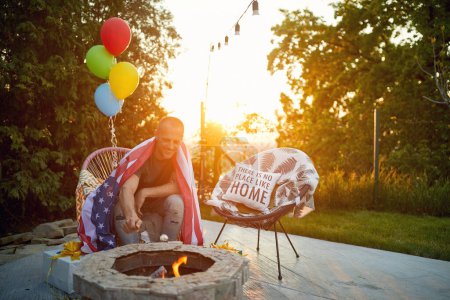 Photo for Middle aged man siting by the fireplace and roasting marshmallows, enjoying holiday outdoors. Sunny summer day, independence day, fourth of july concept. - Royalty Free Image