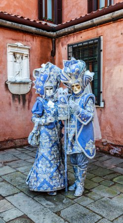 Téléchargez les photos : Venice, Italy- February 18, 2012: Environmental portrait of couple disgused in a beautiful old-fashioned style costume posing in a small Venetian sqaure during the Venice Carnival days - en image libre de droit