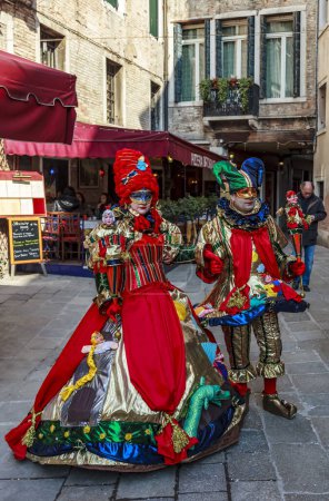 Téléchargez les photos : Venice, Italy- February 18, 2012: Environmental portrait of couple disgused in jester style costumes posing in a small Venetian sqaure during the Venice Carnival days - en image libre de droit