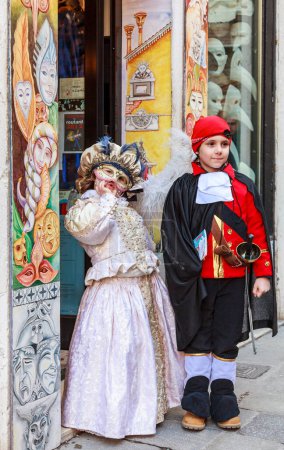 Foto de Venecia, Italia- 18 de febrero de 2012: Imagen de una pareja de niños disfrazados posando frente a una tienda tradicional, durante los días del Carnaval de Venecia - Imagen libre de derechos