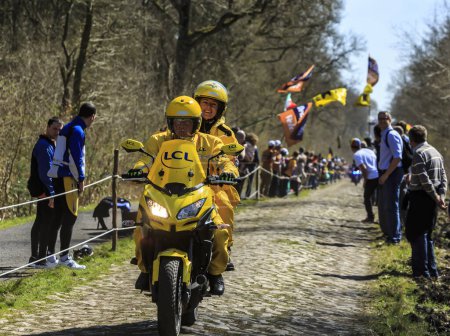 Foto de Wallers-Arenberg, Francia - 12 de abril de 2015: El cronometrador amarillo LCL conduce en el famoso sector pavimentado, The Arenberg gap (Trouee d 'Arenberg), antes del paso de los ciclistas durante la carrera ciclista París-Roubaix. - Imagen libre de derechos