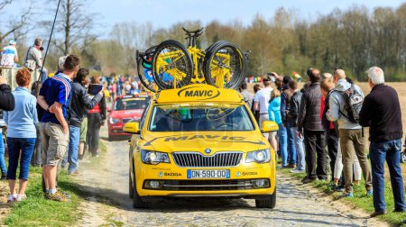 Foto de Carrefour de l 'Arbre, Francia - 12 de abril de 2015: El coche de servicio amarillo de Mavic conduce por la carretera adoquinada del famoso sector Careffour de l' Arbre durante la carrera París-Roubaix en 2015. - Imagen libre de derechos