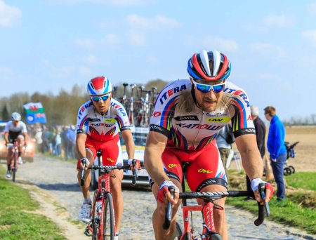 Foto de Carrefour de l 'Arbre, Francia - 12 de abril de 2015: El ciclista austriaco Marco Haller del Team Katusha, montando en el pelotón en el famoso sector Careffour de l' Arbre durante la carrera París-Roubaix en 2015. - Imagen libre de derechos