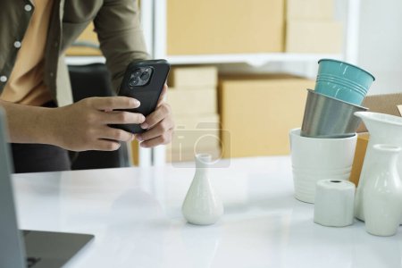 Photo for Asian male online business owner or online store owner using cellphone taking picture and checking parcel box, scanning retail package parcel barcode on shipping box preparing for delivery and shipment. - Royalty Free Image