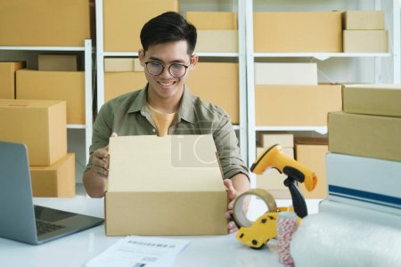 Photo for Asian male small online business owner packing boxes on table and checking retail order preparing for shipment. Online business, e-commerce concept. - Royalty Free Image