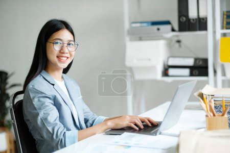 Téléchargez les photos : Sourire asiatique femme d'affaires en ligne travaillant sur ordinateur portable au bureau à la maison. Jeune fille asiatique étudiant ou enseignant à distance à l'aide de l'ordinateur en ligne étudier, formation virtuelle, regarder l'éducation en ligne webinaire au bureau à domicile. - en image libre de droit