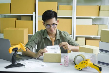 Photo for Young small business entrepreneur man, online store onwer with shelves of cardboard boxes in the background packing product in mailing box, labeling delivery package for shipping to customer. Online - Royalty Free Image