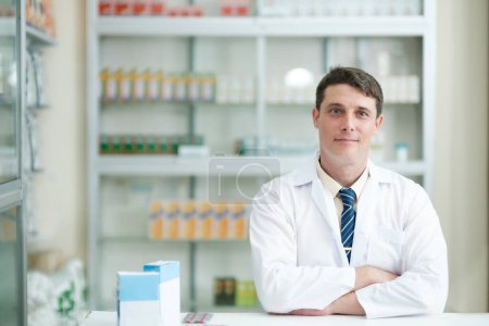 Téléchargez les photos : Homme intelligent jeune adulte pharmacien en robe blanche professionnelle travaillant au bureau dans la pharmacie moderne, pharmacie regardant gentiment la caméra. Médecine et concept de santé. - en image libre de droit