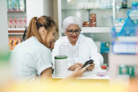 Photo for Female senior pharmacist at the drugstore wearing white gown talking, giving advice, explaining, suggesting, and recommending to client or patient about the prescription and medications. Medicine and - Royalty Free Image
