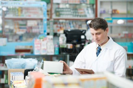 Photo for Male smart young-adult pharmacist in professional white gown looking and checking stock inventory in modern pharmacy, drugstore indoor using tablet. Pharmacy, medicine, and healthcare concept. - Royalty Free Image