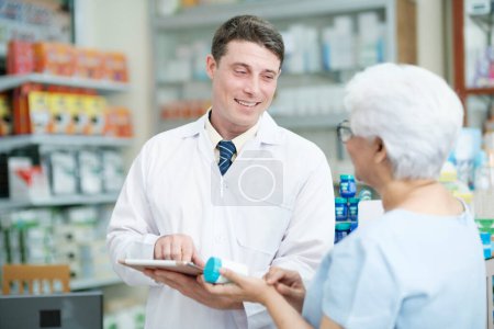 Photo for Smart male pharmacist at the drugstore wearing white gown talking, giving advice, explaining, suggesting, and recommending to client or patient about the prescription and medications. Medicine and - Royalty Free Image