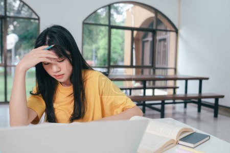 Photo for Asian schoolgirl sitting with her head down Unhappy making a very stressed face at studying for exams. She is tired of having to read a lot of books. - Royalty Free Image