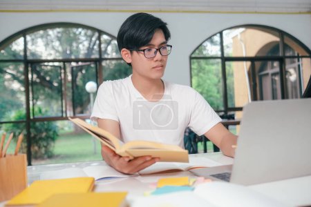 Foto de Joven estudiante universitario asiático está leyendo un libro para los exámenes. El estudiante universitario autoaprendizaje y estudiar en línea en una sala de estudio en la universidad. - Imagen libre de derechos