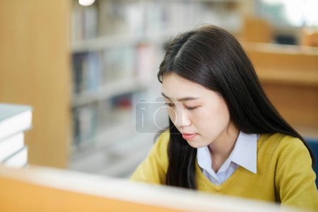 Photo for Young female college highschool student wearing casual clothings sitting at private desk reading book, studying, writing, and doing research for school project at a library. Learning Educational Library concept. - Royalty Free Image