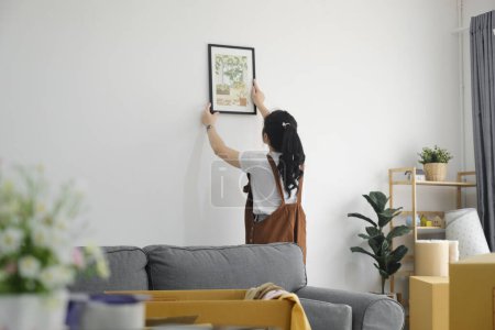 Foto de Mujer asiática joven decorando un nuevo hogar mientras se muda a una nueva casa o apartamento. - Imagen libre de derechos