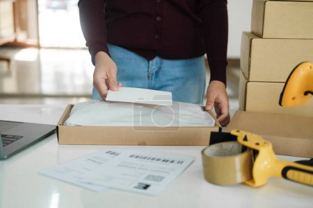 Photo for Close up of young female online business owner standing at table with cardboard boxes and laptop at workplace packing packages to online orders preparing for shipment and delivery to customers. Online - Royalty Free Image