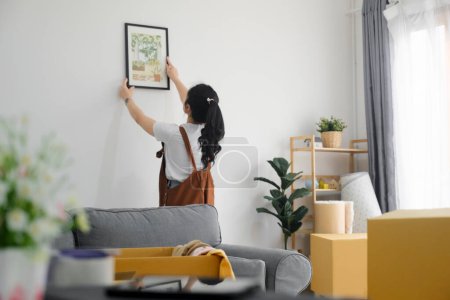 Foto de Mujer asiática joven decorando un nuevo hogar mientras se muda a una nueva casa o apartamento. - Imagen libre de derechos