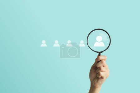 Photo for Hand holding a magnifying glass on light blue background with person icon searching and looking for fitting potential personnel for hiring new employee. Human development, recruitment concept. - Royalty Free Image