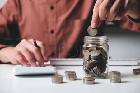 Photo for Close up of businessman hands holding and putting coin into jar for saving, planning and calculating financial plans and strategies for the growth of business, investment, and management. Saving - Royalty Free Image