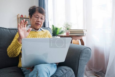 Téléchargez les photos : Les aînés asiatiques souriants adoptent un mode de vie de retraite satisfaisant à la maison, se connectant avec la famille grâce à des vidéoconférences en ligne dynamiques sur leurs ordinateurs portables. Rayonnant de bonheur et de chérir - en image libre de droit