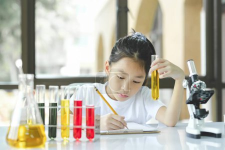 Photo for Little preschool girl is interested in laboratory lesson, taking notes on book for her study. - Royalty Free Image