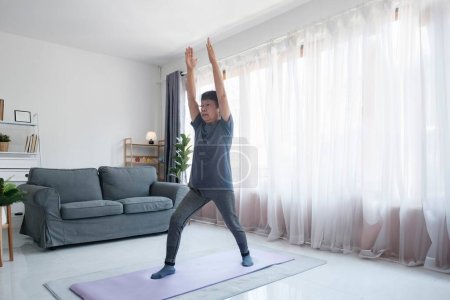 Téléchargez les photos : Mode de vie sain et concept de vieillissement. Équilibre dans la vie. Femme âgée faisant des exercices d'étirement yoga dans le salon à la maison. - en image libre de droit