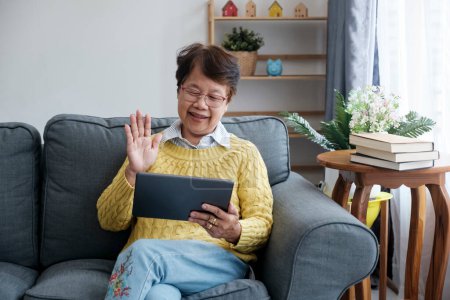 Foto de Las personas mayores asiáticas sonrientes adoptan un estilo de vida de jubilación satisfactorio en el hogar, conectándose con la familia a través de vibrantes videollamadas en línea en su taplet. Radiante felicidad y cariño - Imagen libre de derechos