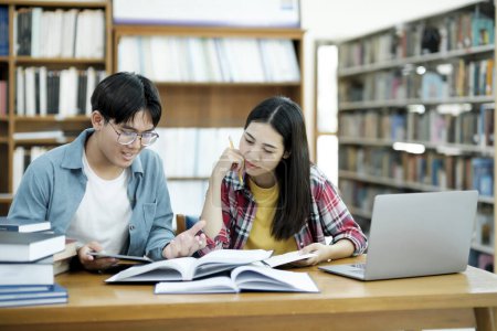 Photo for Young students campus helps friend catching up and learning. University students in cooperation with their assignment at library. Group of young people sitting at table reading books. Education and - Royalty Free Image
