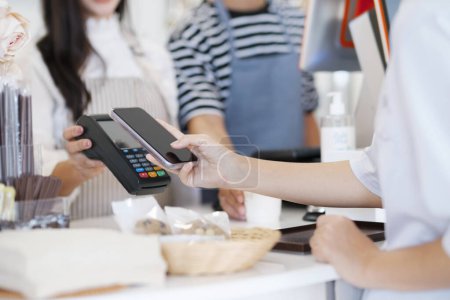 Female customer holding phone near nfc terminal make contactless mobile payment with waitress barista saleswoman on coffeeshop counter, woman client pay in cafe with cellphone via pos machine. Tap-to