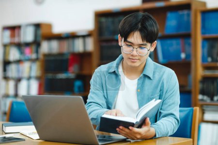 Photo for University Library: Smart asian university student uses Laptop, Writes Notes for Paper, Essay, Study for class assignment. Focused students learning, studying for college exams. - Royalty Free Image