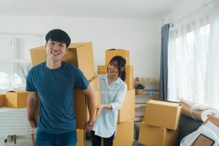 Photo for Asian young happy new married couple moving to their new house or real estate. An attractive romantic man and woman carry boxes parcel with happiness and love. Family moving house relocation concept. - Royalty Free Image