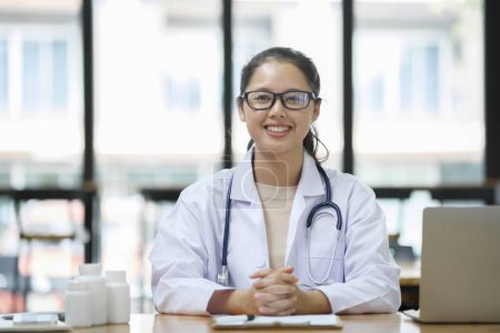Photo for Portrait of happy and successful asian doctor working inside office clinic looking at camera and smiling wearing white coat with stethoscope. - Royalty Free Image