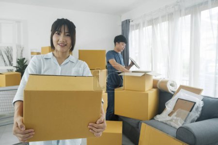 Photo for Asian young happy new married couple moving to their new house or real estate. An attractive romantic man and woman carry boxes parcel with happiness and love. Family moving house relocation concept. - Royalty Free Image