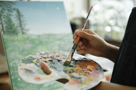 Photo for Young female artist sketches or paints her drawing on canvas in a studio workshop. Teenage girl who likes art and drawing is taking time to create her watercolors on canvas with great intention - Royalty Free Image