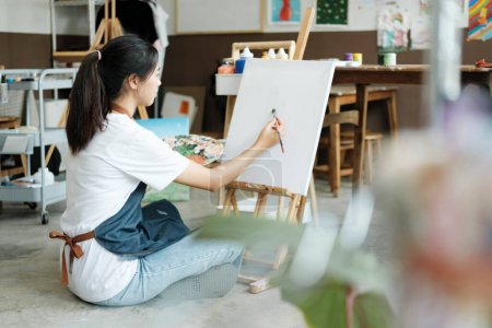 Photo for Young female artist sketches or paints her drawing on canvas in a studio workshop. A teenage girl who likes art and drawing is taking time to create her watercolors on canvas with great intention - Royalty Free Image