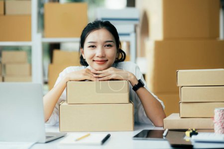 Photo for Young business woman working online e-commerce shopping at her shop. Young woman seller prepare parcel box of product for deliver to customer. Online selling, e-commerce. - Royalty Free Image