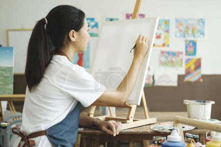 Foto de Joven artista dibuja o pinta su dibujo sobre lienzo en un taller de estudio. Una adolescente a la que le gusta el arte y el dibujo se está tomando el tiempo para crear sus acuarelas sobre lienzo con gran intención - Imagen libre de derechos