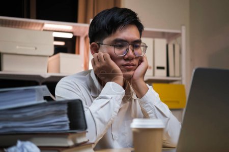 Photo for Asian young tired staff businessman using desktop computer having overwork project overnight in office, exhausted unhappy businessman feeling sleepy after after working hard overtime at night. - Royalty Free Image