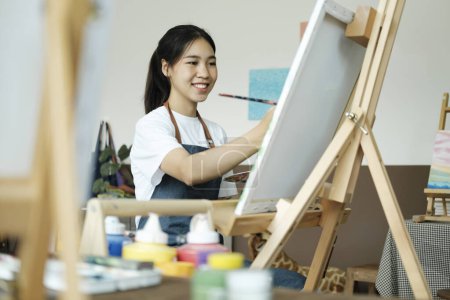 Téléchargez les photos : Jeune artiste féminine dessine ou peint son dessin sur toile dans un atelier. Une adolescente qui aime l'art et le dessin prend le temps de créer ses aquarelles sur toile avec une grande intention - en image libre de droit