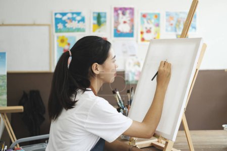 Photo for Young female artist sketches or paints her drawing on canvas in a studio workshop. A teenage girl who likes art and drawing is taking time to create her watercolors on canvas with great intention - Royalty Free Image
