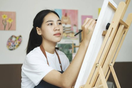 Téléchargez les photos : Jeune artiste féminine dessine ou peint son dessin sur toile dans un atelier. Une adolescente qui aime l'art et le dessin prend le temps de créer ses aquarelles sur toile avec une grande intention - en image libre de droit