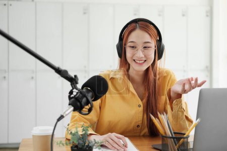 Téléchargez les photos : Femme gaie animant un podcast en direct, s'engageant avec le public en utilisant un microphone professionnel en studio. - en image libre de droit