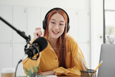 Photo for Cheerful woman hosting a live podcast, engaging with audience using professional microphone in studio. - Royalty Free Image