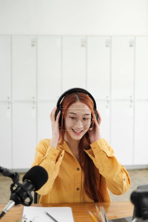 Foto de Mujer alegre hospedando un podcast en vivo, interactuando con la audiencia usando micrófono profesional en el estudio. - Imagen libre de derechos