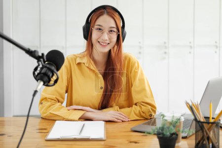 Photo for Woman recording a podcast on her laptop computer with headphones and a microscope. Female podcaster making audio podcast from her home studio. - Royalty Free Image